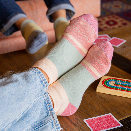 models feet crossed on the coffee table wearing the 6127 Heavyweight No Show featuring the green and pink color block
