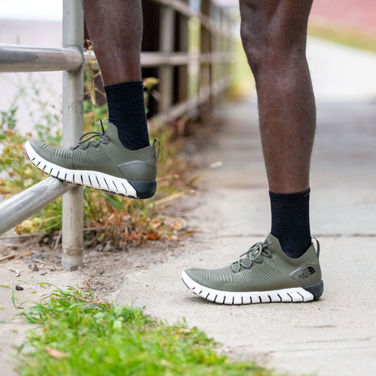 Man resting one foot on a fence, wearing running shoes and Run Micro Crew Ultra-Lightweight Running socks in Black
